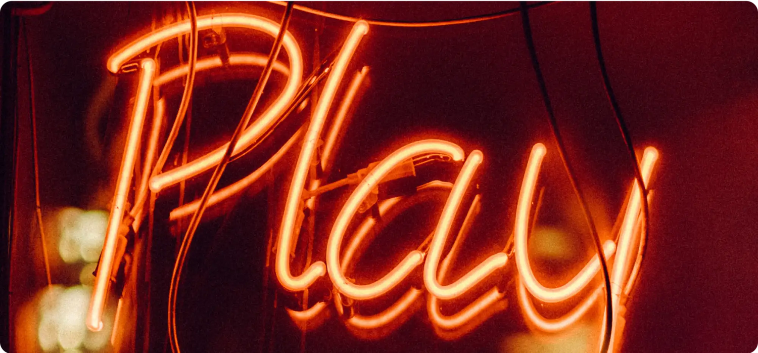 Neonschild „play“ in roten und orangefarbenen Tönen, beleuchtet vor dunklem Hintergrund.
